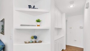 A hallway with white walls, a wooden floor, and a shelf with decorative items. - New Listing University Pastoral (Merced)