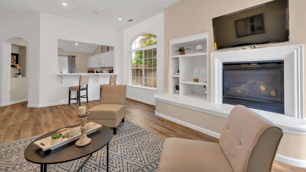 A modern living room with a fireplace, a TV mounted above it, and a dining area with a kitchen in the background. - New Listing University Pastoral (Merced)