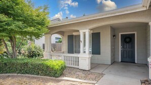 A residential house with a covered porch, a front door with a wreath, and a small garden area with a tree and shrubs. - New Listing University Pastoral (Merced)