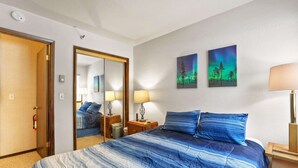 Ett hotellrum med en stor säng, två sänglampor, en spegel och två tavlor med trädmotiv.