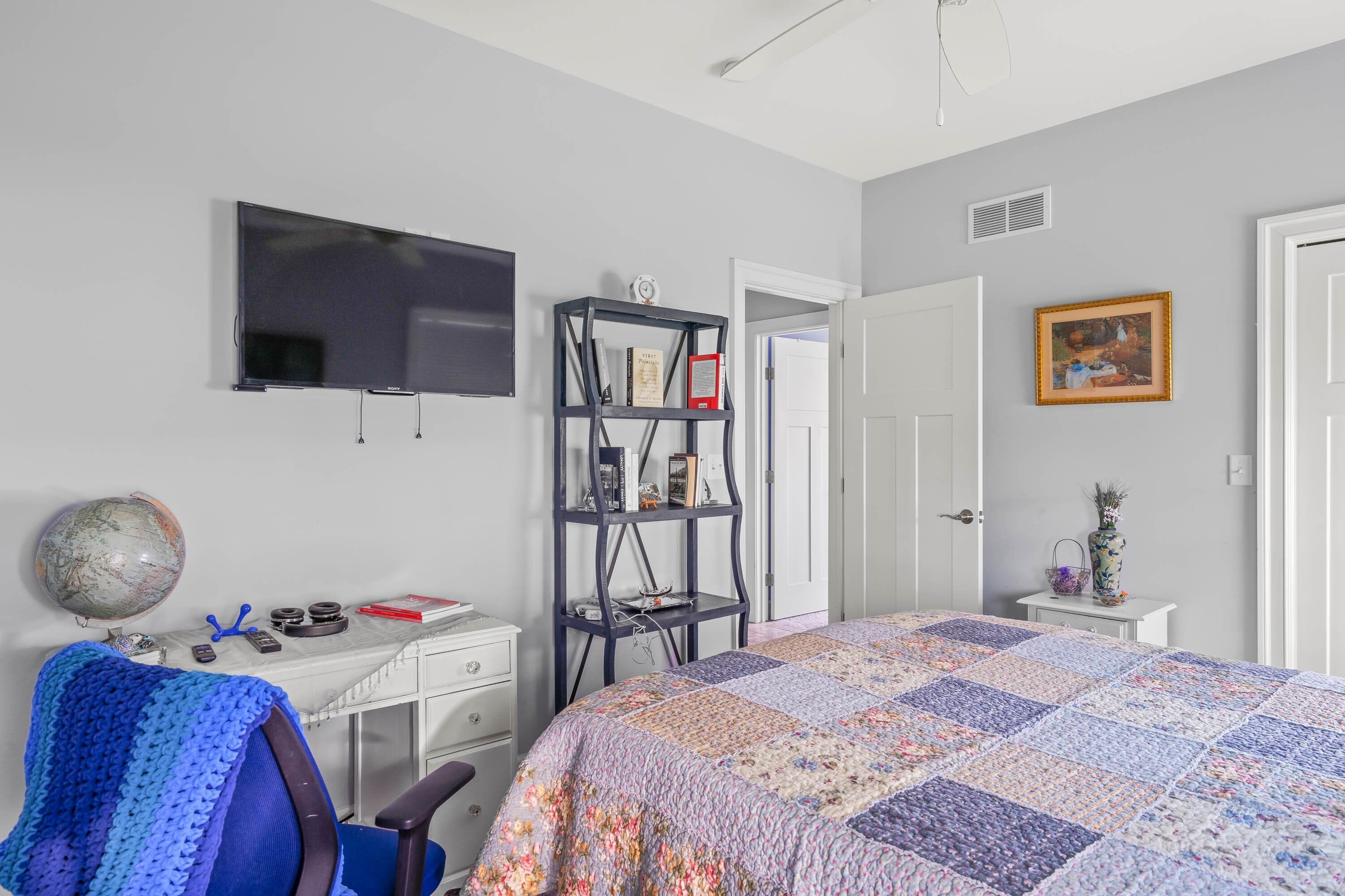 Une chambre à coucher avec un lit, un bureau, une bibliothèque, une télévision et une porte.