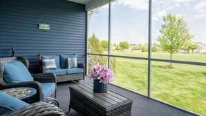 Eine überdachte Veranda mit Korbmöbeln, einem Couchtisch und Blick auf einen Rasen.