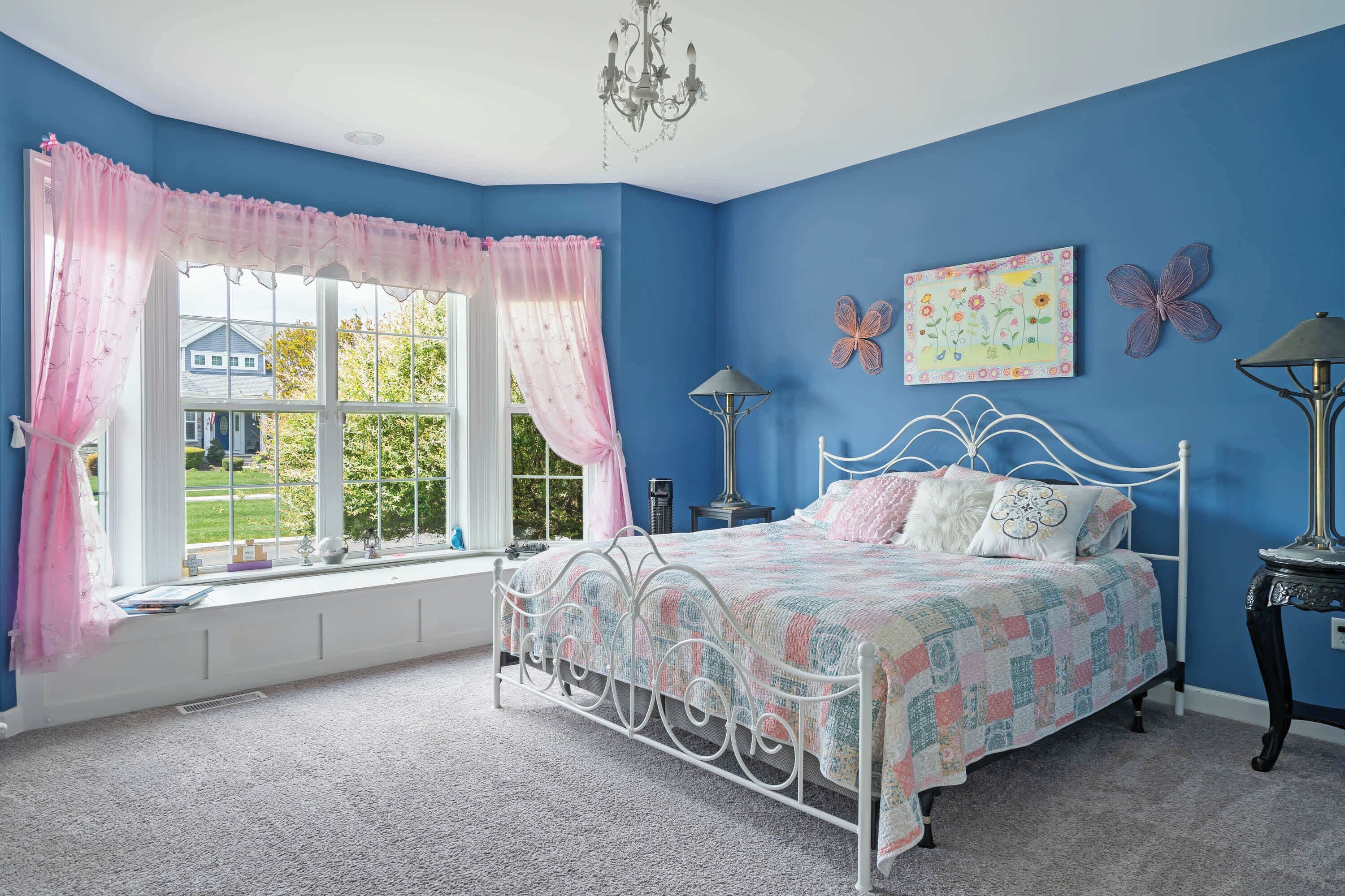 A bedroom with a large window, a bed with a patterned bedspread, and butterfly wall art.