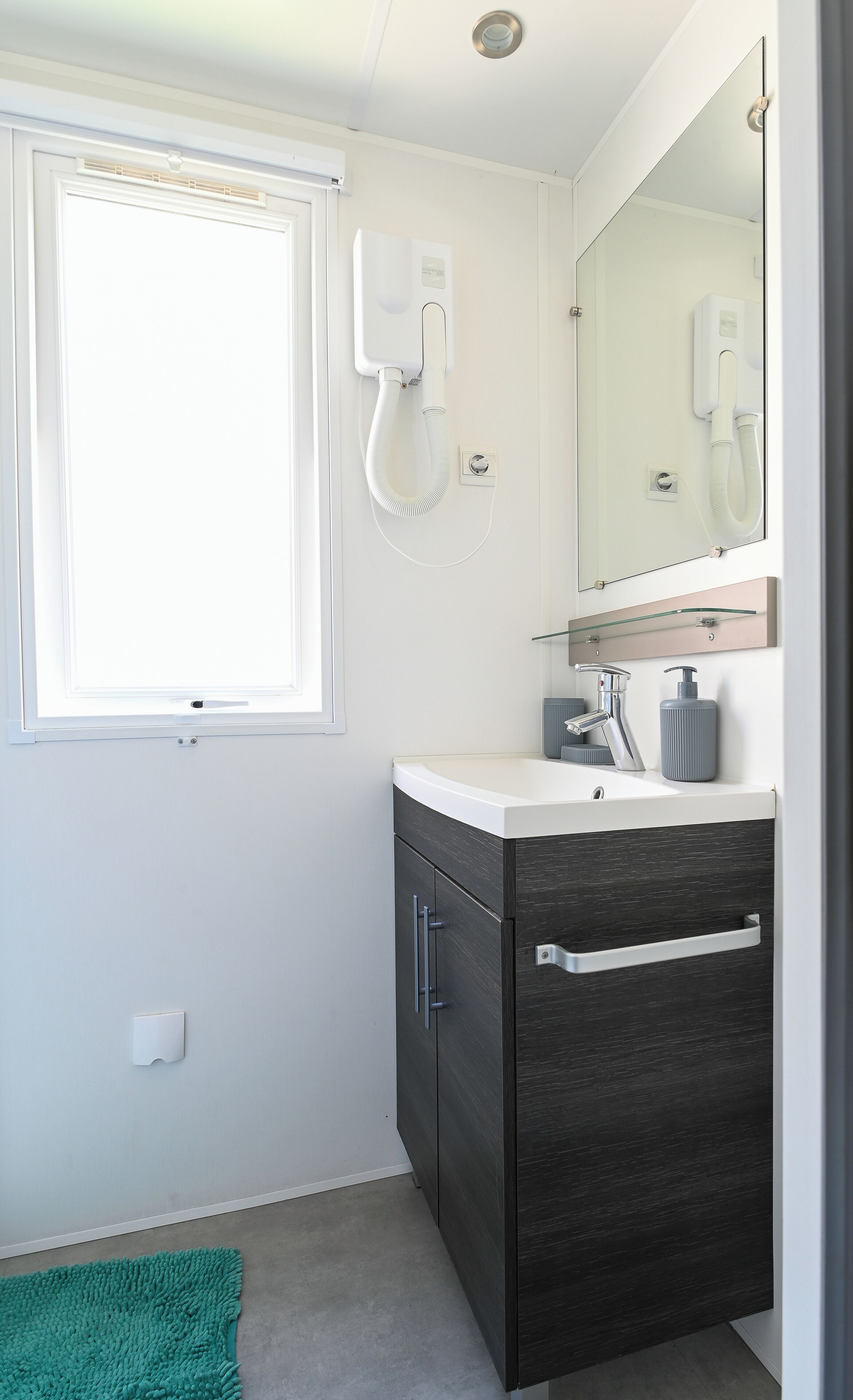 Un baño con tocador blanco, un espejo, una ventana y un teléfono blanco.