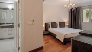 Une chambre moderne avec un plancher en bois, un grand lit recouvert d’une couette blanche, une table de chevet avec une lampe, et une vue sur l’extérieur à travers une fenêtre ornée de rideaux.
