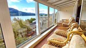 Ein Balkon mit Korbmöbeln und Blick auf einen See und Berge.