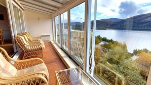 Ein Balkon mit Korbmöbeln und Blick auf einen See und Hügel.