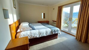 A hotel room with a bed, a nightstand, a mirror, and a view of the outdoors through a sliding glass door.