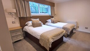A bedroom with two beds, a window with curtains, a radiator, and a bedside table. - Pine Marten Lodge 03 Loch Rannoch Highland Club (Pitlochry)