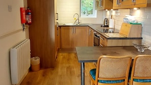 A compact kitchen with wooden cabinets, a dining table with chairs, a radiator, and a fire extinguisher. - Lochside Lodge 07 Loch Rannoch Highland Club (Pitlochry)