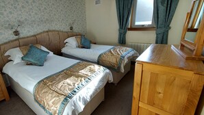 Een slaapkamer met twee bedden, een houten dressoir en een raam met gordijnen.