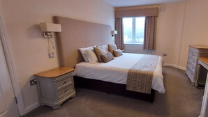 A bedroom with a bed, bedside tables, a dresser, and a window with curtains. - Highland Lodge 41 Loch Rannoch Highland Club (Pitlochry)