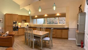 A modern kitchen with wooden cabinets, a dining table with chairs, and pendant lighting. - Highland Lodge 41 Loch Rannoch Highland Club (Pitlochry)