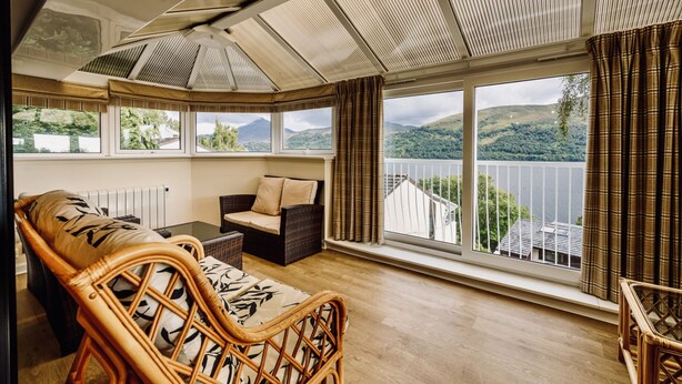 A room with a large window, wicker furniture, and a view of hills. - Highland Lodge 41 Loch Rannoch Highland Club (Pitlochry)