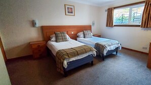 A room with two single beds, a wooden nightstand, a small cabinet, and a window with curtains. - Red Squirrel Lodge 05 Loch Rannoch Highland Club (Pitlochry)