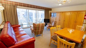 A cozy living room with a red leather sofa, plaid armchairs, a wooden dining table, and a TV. - Red Squirrel Lodge 05 Loch Rannoch Highland Club (Pitlochry)