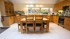 Uma cozinha moderna com armários de madeira, uma mesa de jantar com cadeiras, uma janela grande com vista para o verde e eletrodomésticos embutidos.