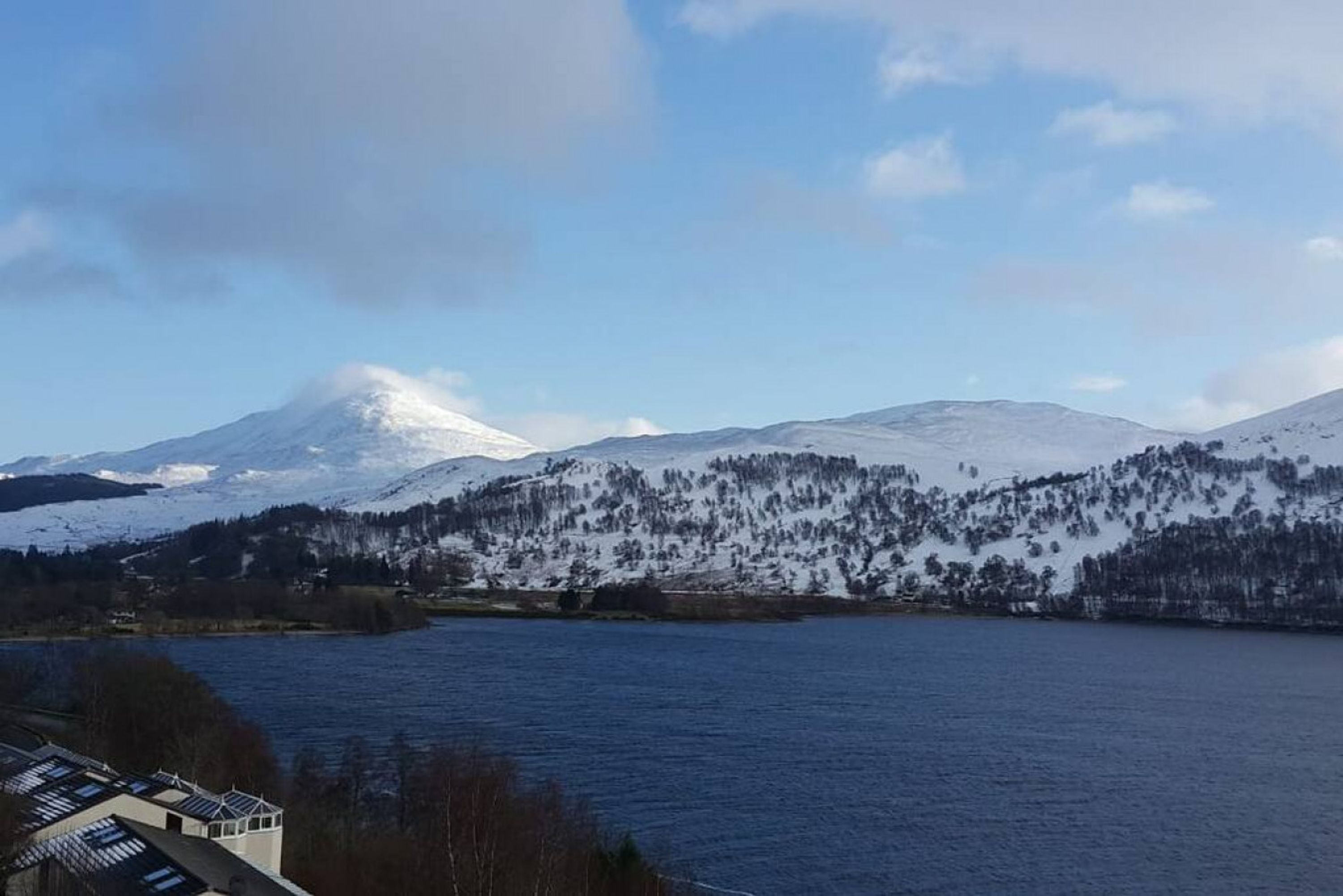 Un lago con montañas nevadas al fondo y un edificio con techo inclinado en primer plano.