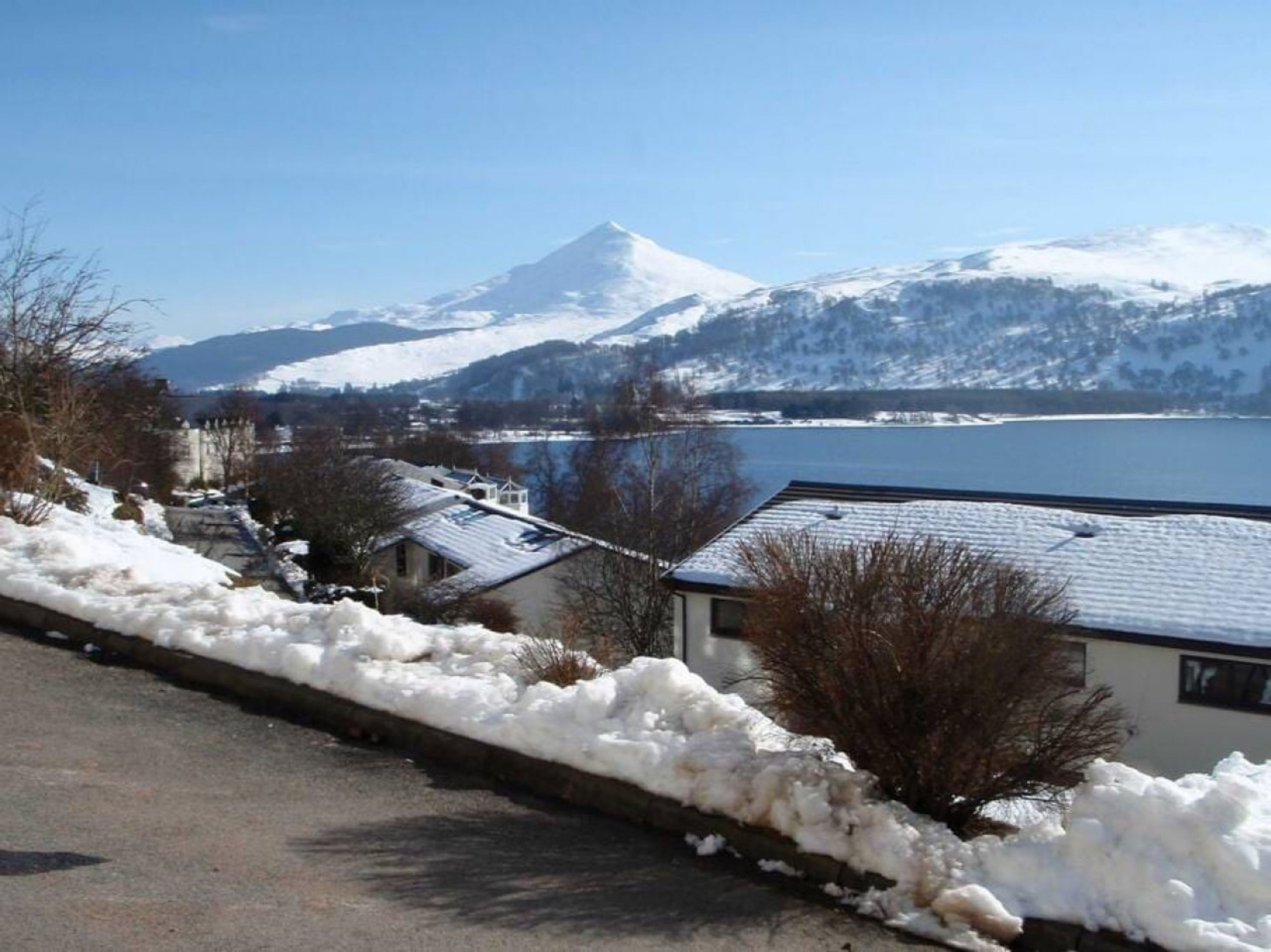 A snow-covered landscape with a mountain in the background, a body of water, and buildings along a road.