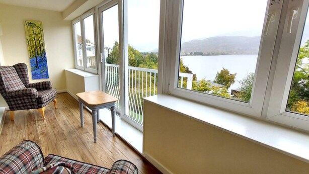 Un balcone con vista su un lago, un divano a quadri, una sedia e un tavolino.