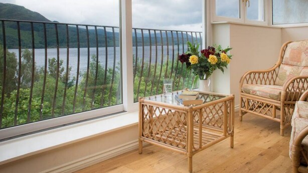 Un balcon avec vue sur un lac et des montagnes, une table en osier et deux chaises en osier.