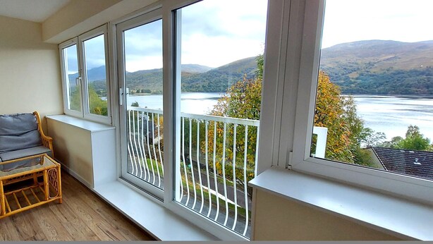 A balcony with a sofa and a small table, overlooking a lake and hills. - Red Deer Lodge 05 Loch Rannoch Highland Club (Pitlochry)