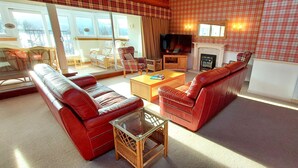 A living room with a red sofa, a glass coffee table, a fireplace, and a television. - Highland Lodge 09 Loch Rannoch Highland Club (Pitlochry)