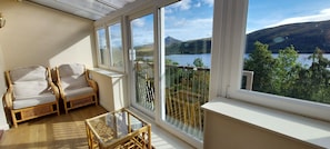 A balcony with wicker furniture, a glass coffee table, and a view of a lake and mountains. - Red Squirrel Lodge 04 Loch Rannoch Highland Club (Pitlochry)