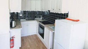A compact kitchen with white cabinets, a microwave, a stove, and a refrigerator. - Apartment 09 Loch Rannoch Highland Club (Pitlochry)