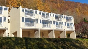A multi-story building with balconies, set against a backdrop of autumn-colored trees. - Studio 06 Loch Rannoch Highland Club (Pitlochry)