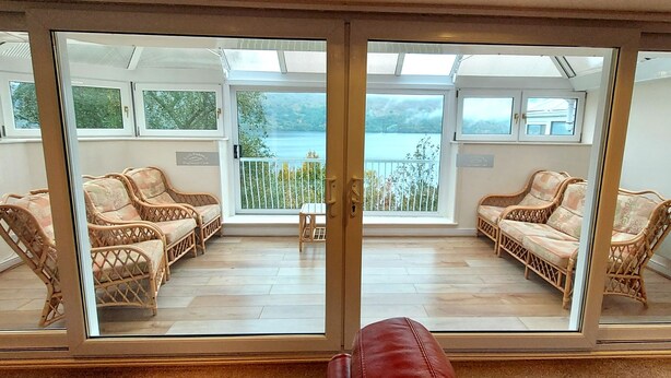 Ein Zimmer mit Korbmöbeln, eine Glastür zu einem Balkon mit Blick auf einen See und Berge.