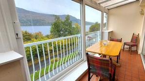 Un balcon avec une table et des chaises, donnant sur un lac et des collines.