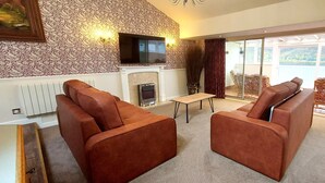A living room with two brown sofas, a small table, a fireplace, and a TV mounted on a patterned wall. - Highland Lodge 36 Loch Rannoch Highland Club (Pitlochry)