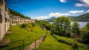 A hotel with a grassy lawn, a pathway, and a view of a lake and mountains. - Studio 05 Loch Rannoch Highland Club (Pitlochry)