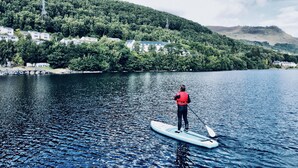 A person paddleboarding on a calm lake with a forested hillside in the background. - Studio 05 Loch Rannoch Highland Club (Pitlochry)