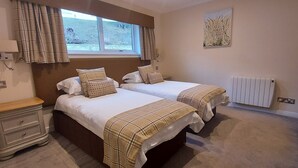 A bedroom with two beds, a window with curtains, a radiator, and a bedside table. - Pine Marten Lodge 08 Loch Rannoch Highland Club (Pitlochry)