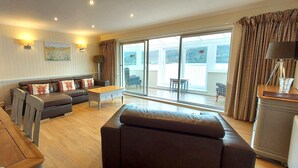 A modern living room with a sofa, a dining table, and a kitchen area with built-in appliances. - Pine Marten Lodge 08 Loch Rannoch Highland Club (Pitlochry)