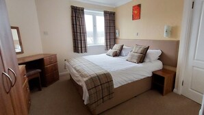 A bedroom with a bed, bedside tables, a dresser, a window with curtains, and a wall-mounted light fixture. - Highland Lodge 02 Loch Rannoch Highland Club (Pitlochry)