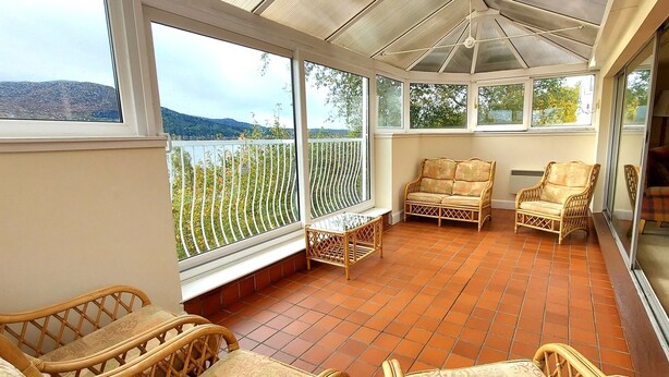 A covered patio with wicker furniture, large windows, and a view of hills. - Highland Lodge 02 Loch Rannoch Highland Club (Pitlochry)
