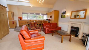 A spacious living room with leather sofas, a wooden coffee table, and a fireplace. - Highland Lodge 02 Loch Rannoch Highland Club (Pitlochry)