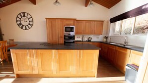 A kitchen with wooden cabinets, a central island, a clock, and a window with a view. - Highland Lodge 35 Loch Rannoch Highland Club (Pitlochry)
