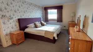 A bedroom with a bed, wooden nightstands, a dresser, a window with curtains, and a wall with a floral wallpaper pattern. - Highland Lodge 35 Loch Rannoch Highland Club (Pitlochry)
