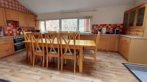 A kitchen with wooden cabinets, a dining table with chairs, and a red leather chair. - Highland Lodge 46 Loch Rannoch Highland Club (Pitlochry)