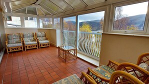 A sunroom with wicker furniture, large windows, and a view of hills. - Highland Lodge 46 Loch Rannoch Highland Club (Pitlochry)