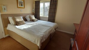A bedroom with a bed, pillows, a window with curtains, a door, and a wall-mounted light switch. - Highland Lodge 46 Loch Rannoch Highland Club (Pitlochry)