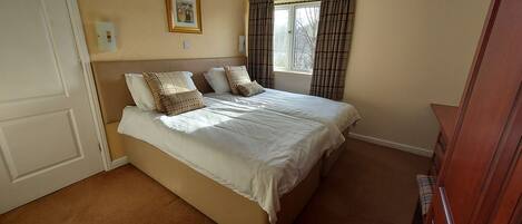 A bedroom with a bed, pillows, a window with curtains, a door, and a wall-mounted light switch.