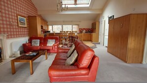 A spacious living room with a fireplace, red leather sofa, and a dining area with wooden furniture. - Highland Lodge 46 Loch Rannoch Highland Club (Pitlochry)