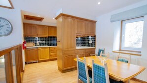 A kitchen with wooden cabinets, a tiled backsplash, and a dining area with a table and chairs. - Lochside Lodge 03 Loch Rannoch Highland Club (Pitlochry)