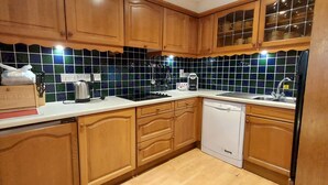 A kitchen with wooden cabinets, a tiled backsplash, a kettle, a coffee maker, and a dishwasher. - Lochside Lodge 03 Loch Rannoch Highland Club (Pitlochry)