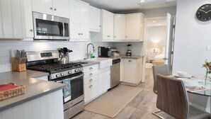A modern kitchen with white cabinetry, stainless steel appliances, and a dining area with a glass table and wooden chair. - 1BR House in Glendale With Private Fenced Yard p55 (Glendale)